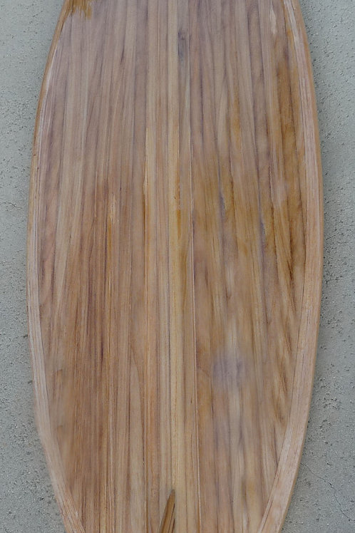 A wooden surfboard-shaped panel with visible wood grain in tan and brown tones, photographed on a concrete surface