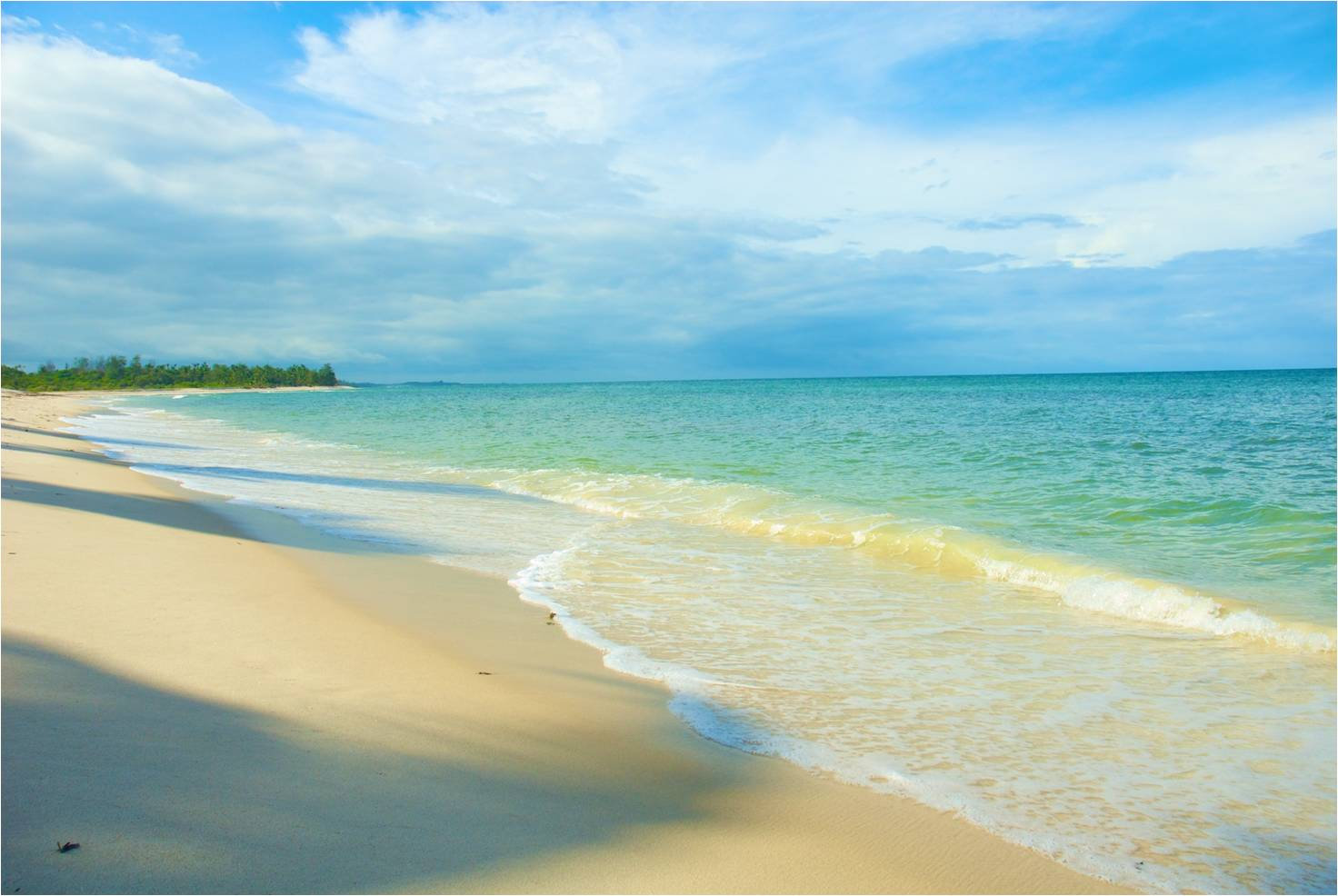 A sandy beach shoreline with gentle turquoise waves, blue sky with clouds, and distant tree line, calm and serene mood